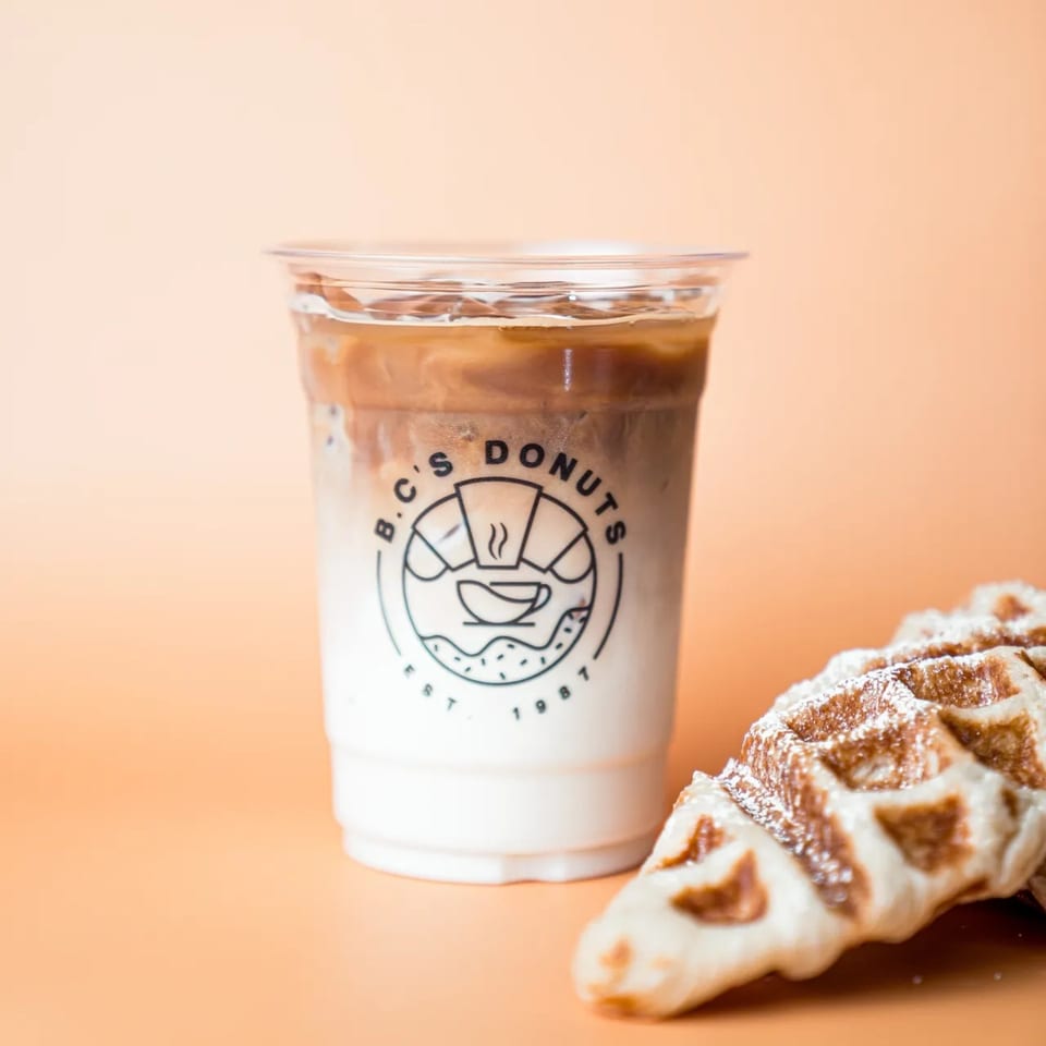 Iced coffee with B.C's Donuts logo next to a powdered sugar waffle on an orange background.