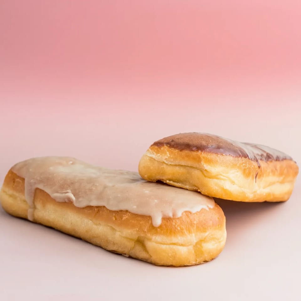 Two B.C's Donuts, one with white glaze and one with chocolate glaze, on a pink background.