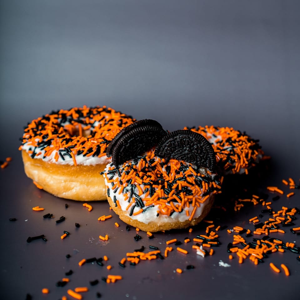 Three B.C's Donuts with white frosting, orange and black sprinkles, and Oreo pieces.