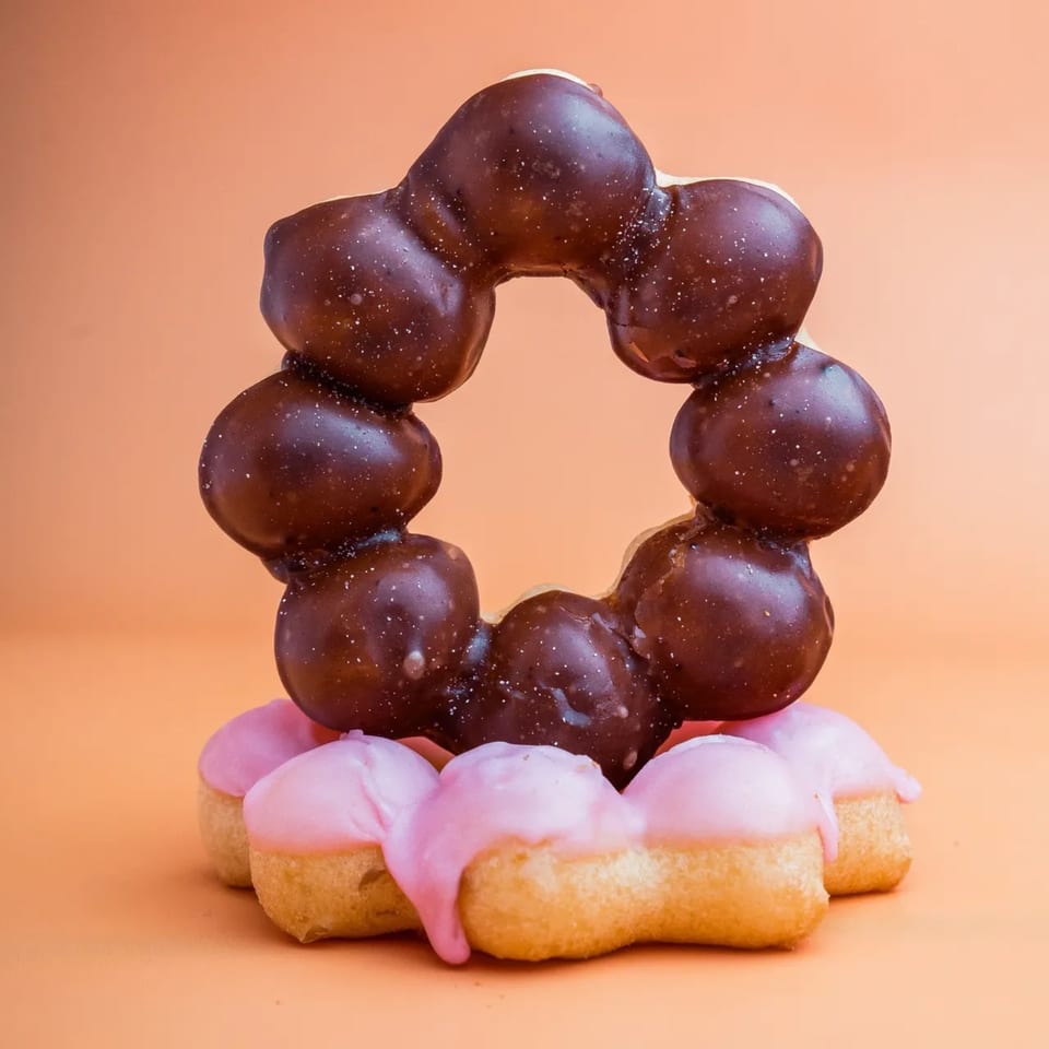 Two B.C's Donuts, one chocolate-glazed and one pink-glazed, stacked on an orange background.